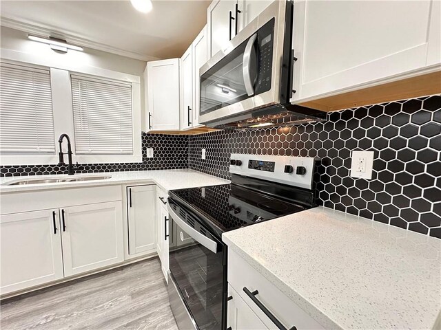 kitchen featuring appliances with stainless steel finishes, decorative backsplash, white cabinets, light wood-type flooring, and sink