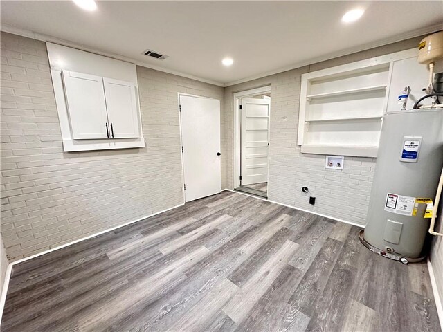 washroom with brick wall, electric water heater, and dark wood-type flooring