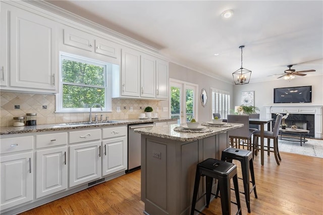 kitchen with dishwasher, a sink, white cabinets, a breakfast bar, and light wood-style floors
