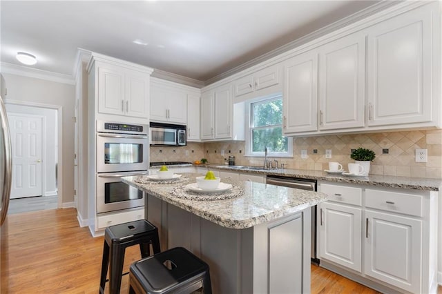 kitchen with appliances with stainless steel finishes, a kitchen breakfast bar, white cabinets, crown molding, and tasteful backsplash