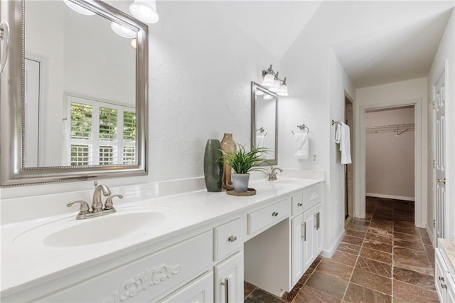 bathroom featuring double vanity, a walk in closet, and vaulted ceiling