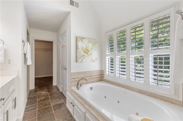 full bathroom with healthy amount of natural light, vanity, a whirlpool tub, lofted ceiling, and a spacious closet