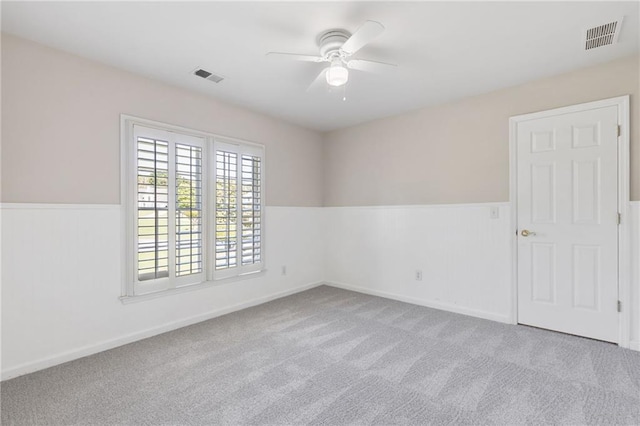 carpeted empty room featuring ceiling fan and a wainscoted wall