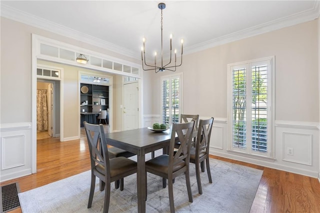 dining space featuring a chandelier, ornamental molding, healthy amount of natural light, wainscoting, and light wood-style flooring