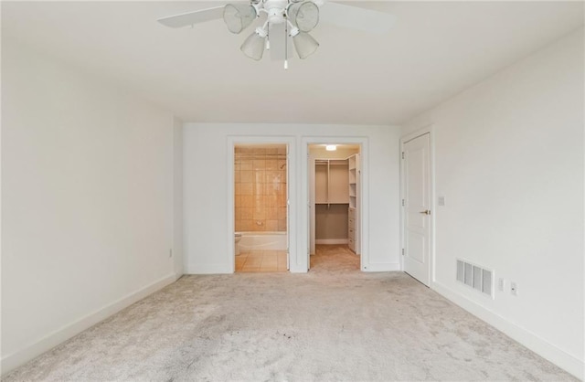 unfurnished bedroom featuring connected bathroom, ceiling fan, light colored carpet, a walk in closet, and a closet