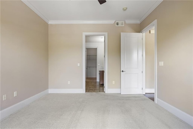 unfurnished bedroom featuring carpet floors, ornamental molding, a spacious closet, baseboards, and ceiling fan