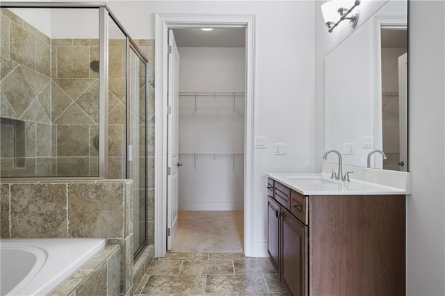 bathroom featuring a shower stall, vanity, a spacious closet, tiled bath, and baseboards