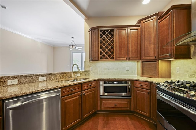 kitchen with stainless steel appliances, wall chimney range hood, a sink, dark wood-style flooring, and light stone countertops