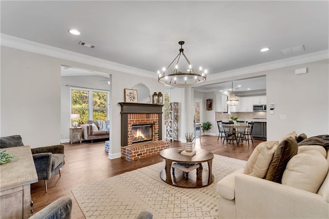 living room featuring ornamental molding, a chandelier, hardwood / wood-style floors, and a fireplace