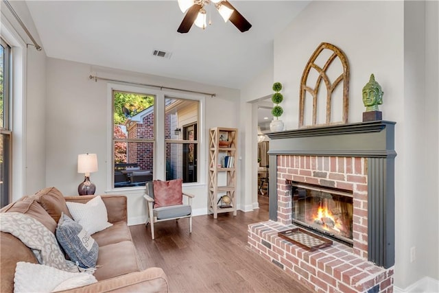 living room with vaulted ceiling, a brick fireplace, ceiling fan, and wood-type flooring