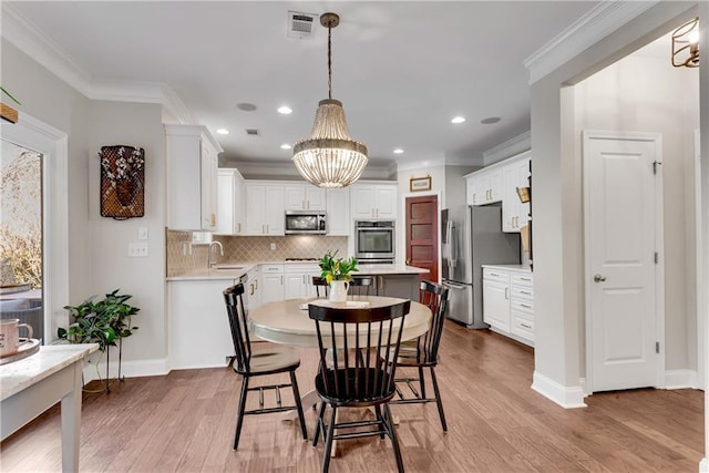 dining space with light wood-type flooring, ornamental molding, and a chandelier