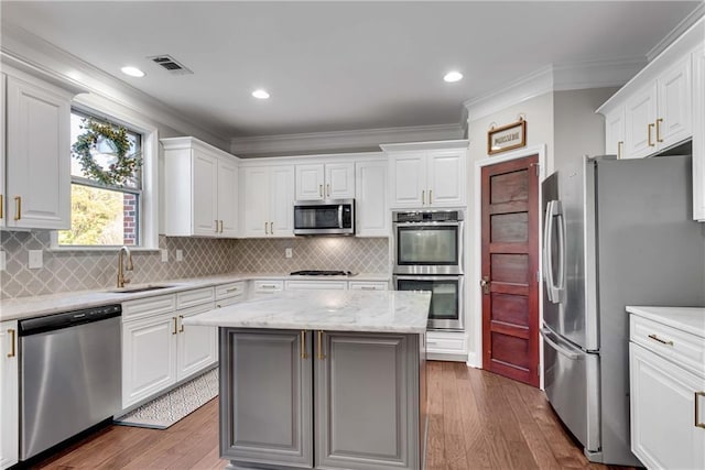 kitchen with stainless steel appliances, a center island, light stone counters, white cabinets, and sink