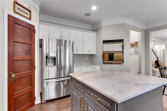 kitchen with white cabinets, stainless steel fridge with ice dispenser, light stone countertops, a kitchen island, and gray cabinetry