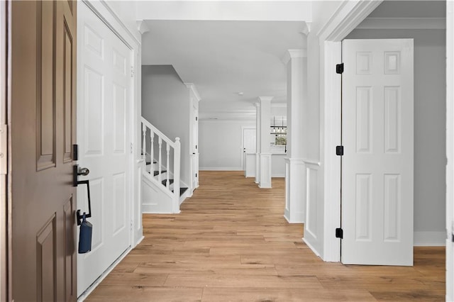 foyer entrance with light wood-style flooring, stairs, ornamental molding, and baseboards