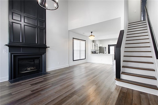 unfurnished living room with an inviting chandelier, a large fireplace, dark hardwood / wood-style floors, and a high ceiling