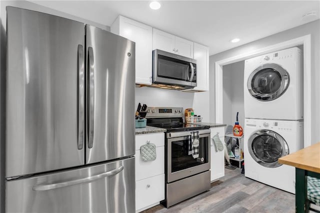 kitchen with appliances with stainless steel finishes, dark stone counters, stacked washing maching and dryer, light hardwood / wood-style floors, and white cabinets