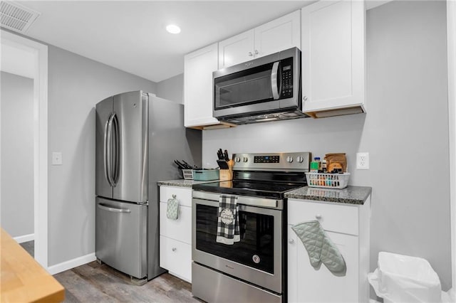 kitchen with stainless steel appliances, dark wood-type flooring, white cabinets, and dark stone counters