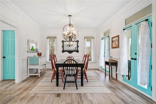 dining space with a chandelier, light wood-type flooring, french doors, a decorative wall, and ornamental molding