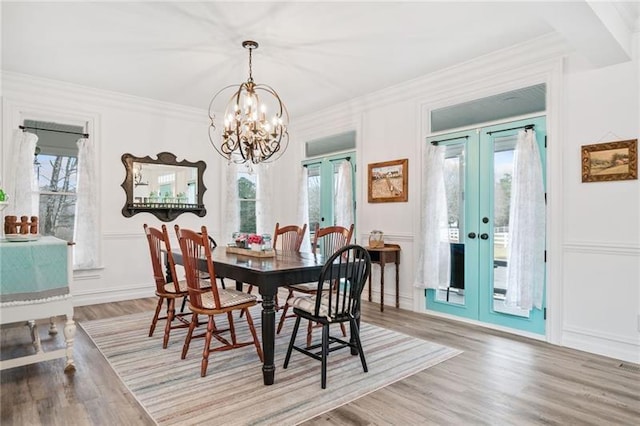 dining space with french doors, crown molding, wood finished floors, a chandelier, and a decorative wall