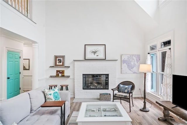 living area featuring a high ceiling, wood finished floors, a brick fireplace, and baseboards