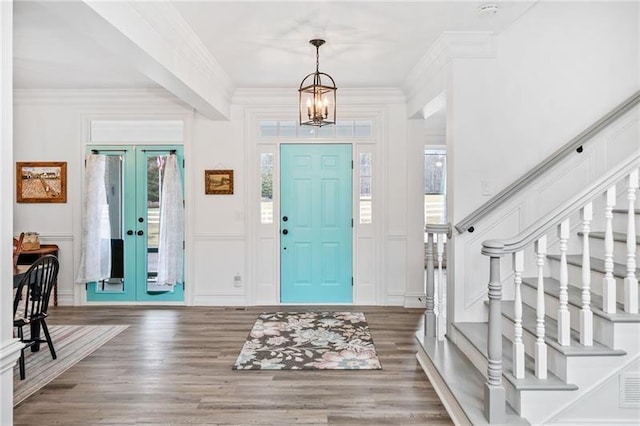 entryway with a decorative wall, wood finished floors, french doors, a chandelier, and crown molding