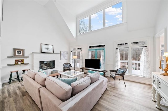 living room with high vaulted ceiling, wood finished floors, and a brick fireplace