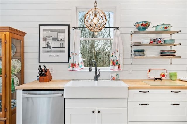 kitchen with dishwasher, butcher block countertops, a sink, wood walls, and white cabinetry
