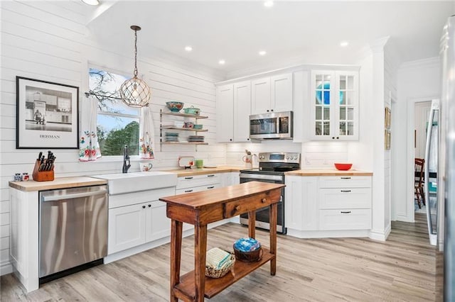 kitchen with stainless steel appliances, a sink, white cabinetry, light wood finished floors, and ornamental molding