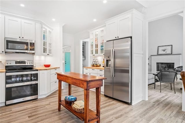 kitchen featuring stainless steel appliances, white cabinets, light wood finished floors, glass insert cabinets, and crown molding