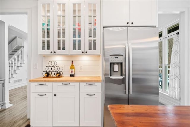 kitchen with butcher block counters, stainless steel refrigerator with ice dispenser, glass insert cabinets, white cabinets, and wood finished floors