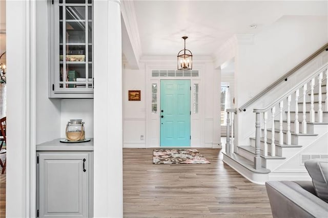 entryway featuring light wood-style flooring, a decorative wall, stairs, and ornamental molding