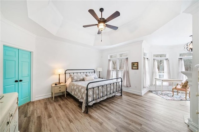 bedroom with a raised ceiling, light wood-style floors, baseboards, ornamental molding, and ceiling fan