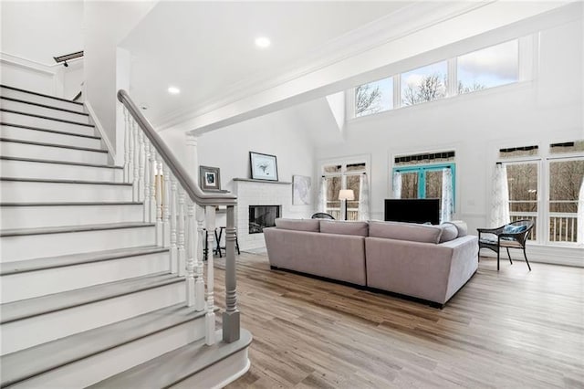 living area with stairs, healthy amount of natural light, a fireplace, light wood-style flooring, and a high ceiling