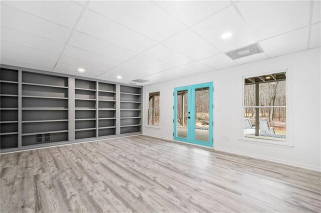 empty room featuring a drop ceiling, built in features, wood finished floors, french doors, and baseboards