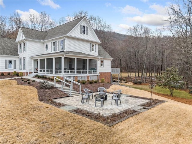 view of front of home with a sunroom, an outdoor fire pit, a patio area, and a shingled roof