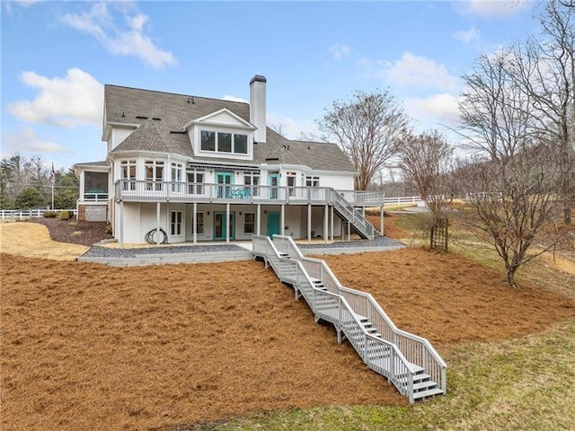 rear view of property featuring stairway, a sunroom, a chimney, a deck, and a lawn