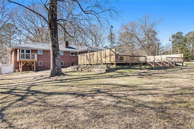 rear view of property featuring brick siding, a yard, a chimney, and a wooden deck