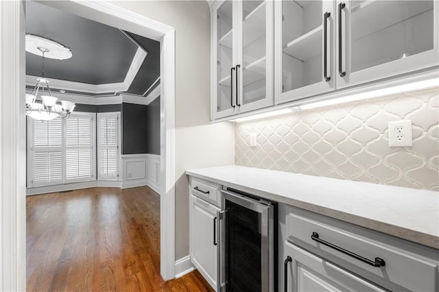 bar featuring wine cooler, dark wood-style flooring, ornamental molding, wainscoting, and a chandelier