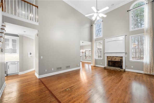 unfurnished living room featuring ceiling fan with notable chandelier, a stone fireplace, light wood-type flooring, and baseboards