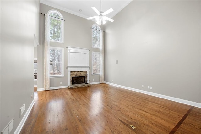 unfurnished living room with baseboards, visible vents, wood finished floors, a high ceiling, and a stone fireplace