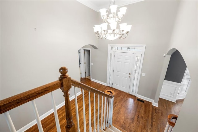 foyer entrance featuring a towering ceiling, arched walkways, a chandelier, and wood finished floors