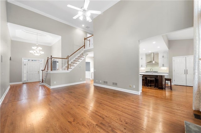 unfurnished living room with stairs, a high ceiling, wood finished floors, and ornamental molding