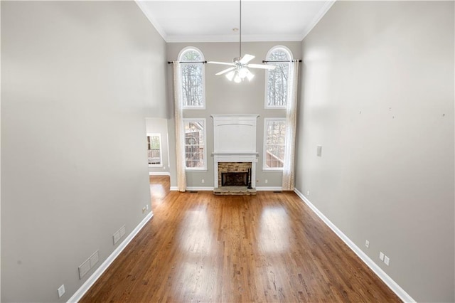 unfurnished living room featuring ceiling fan, a stone fireplace, wood finished floors, baseboards, and ornamental molding