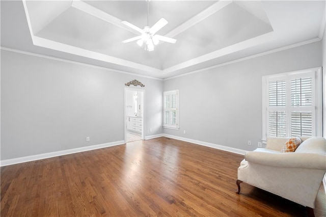 living area with a ceiling fan, a tray ceiling, baseboards, and wood finished floors