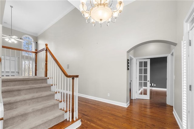 staircase featuring high vaulted ceiling, arched walkways, baseboards, and wood finished floors