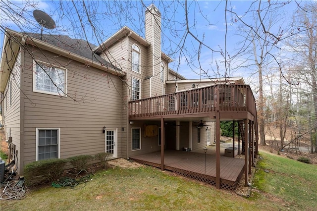 back of property with a chimney, a wooden deck, and a lawn