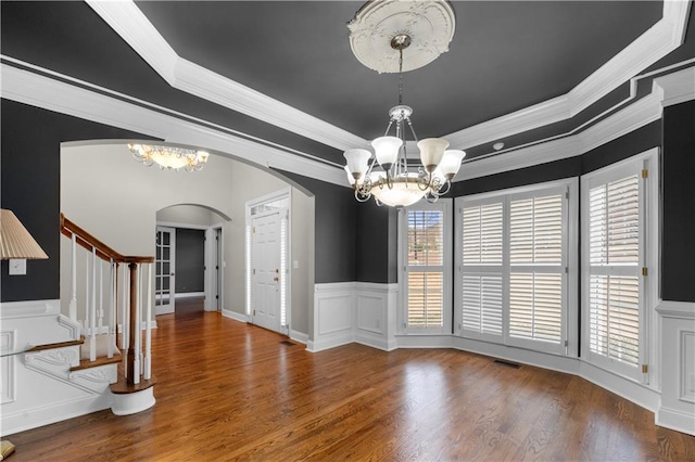 interior space with arched walkways, a raised ceiling, wood finished floors, stairs, and a chandelier