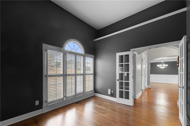 spare room featuring arched walkways, french doors, visible vents, an inviting chandelier, and wood finished floors