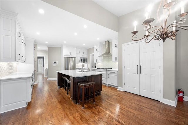 kitchen with wall chimney exhaust hood, white cabinetry, stainless steel appliances, and a sink