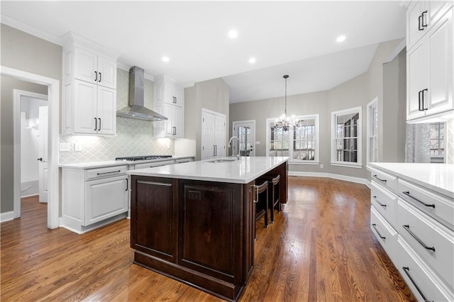 kitchen with tasteful backsplash, light countertops, white cabinetry, a sink, and wall chimney range hood